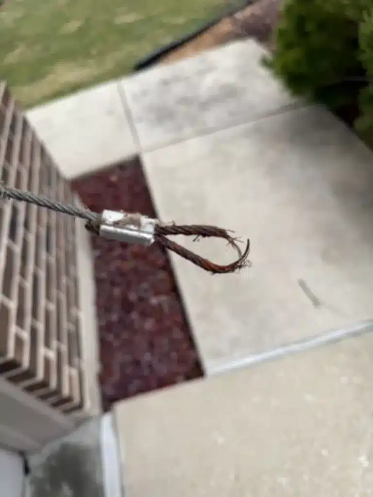 A close-up of a frayed and snapped steel garage door lift cable with a loop end.
