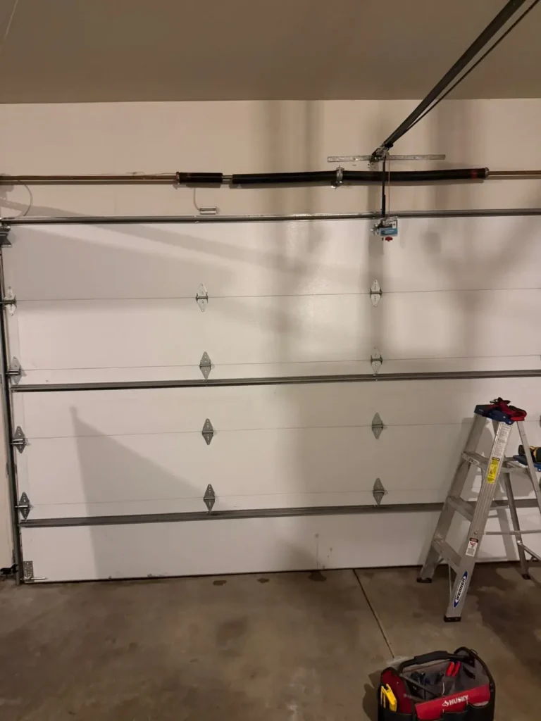 A wide shot of a white four-panel garage door inside a garage with a step-ladder positioned to the right.