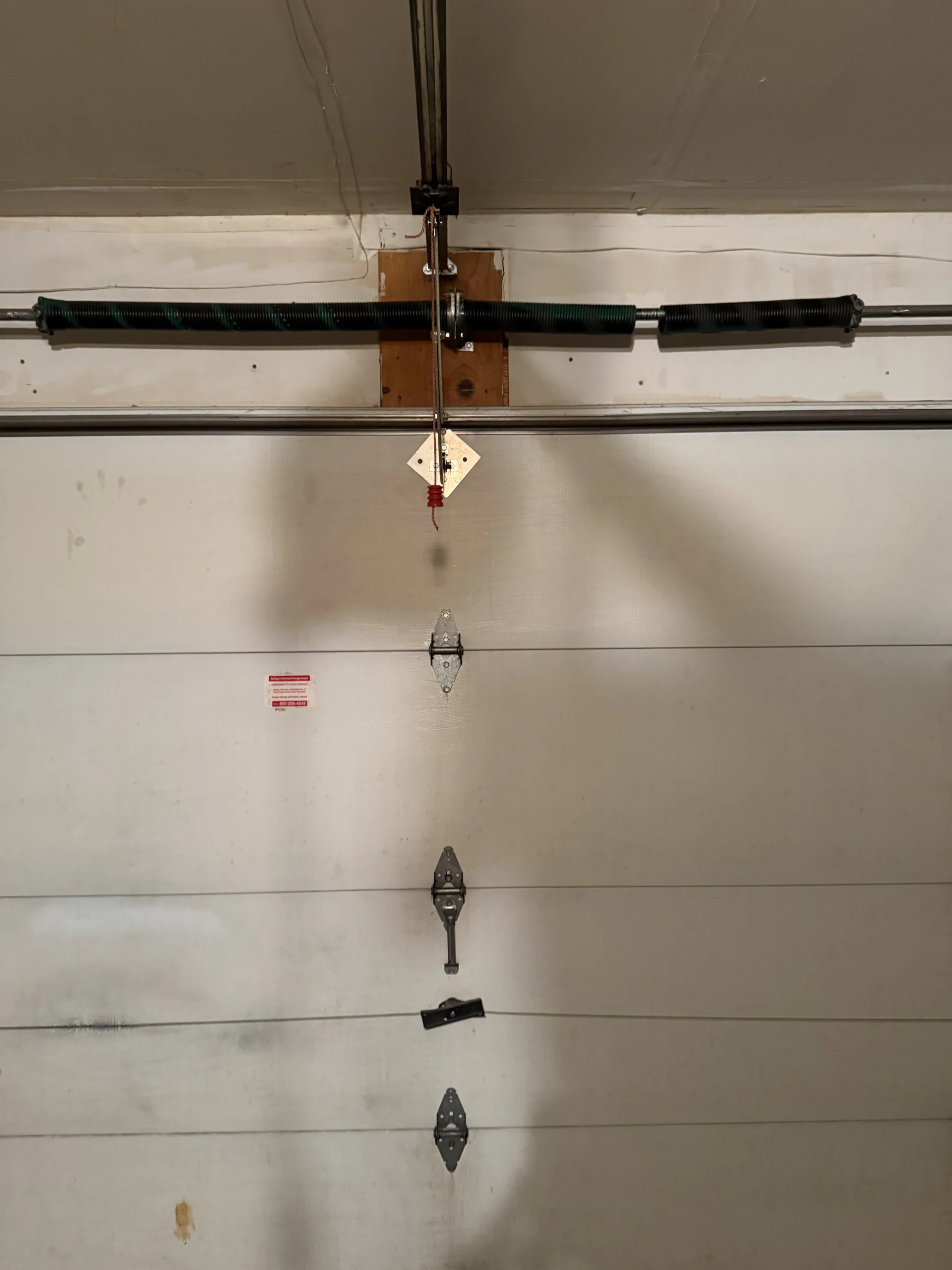 Close-up view of a garage door overhead torsion spring bar, center bearing, and cables.